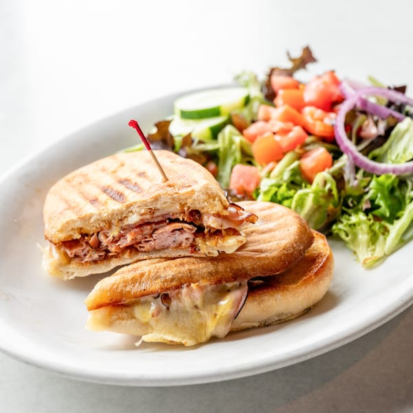 A grilled panini sandwich, cut in half, with melted cheese and meat, served with a side salad.