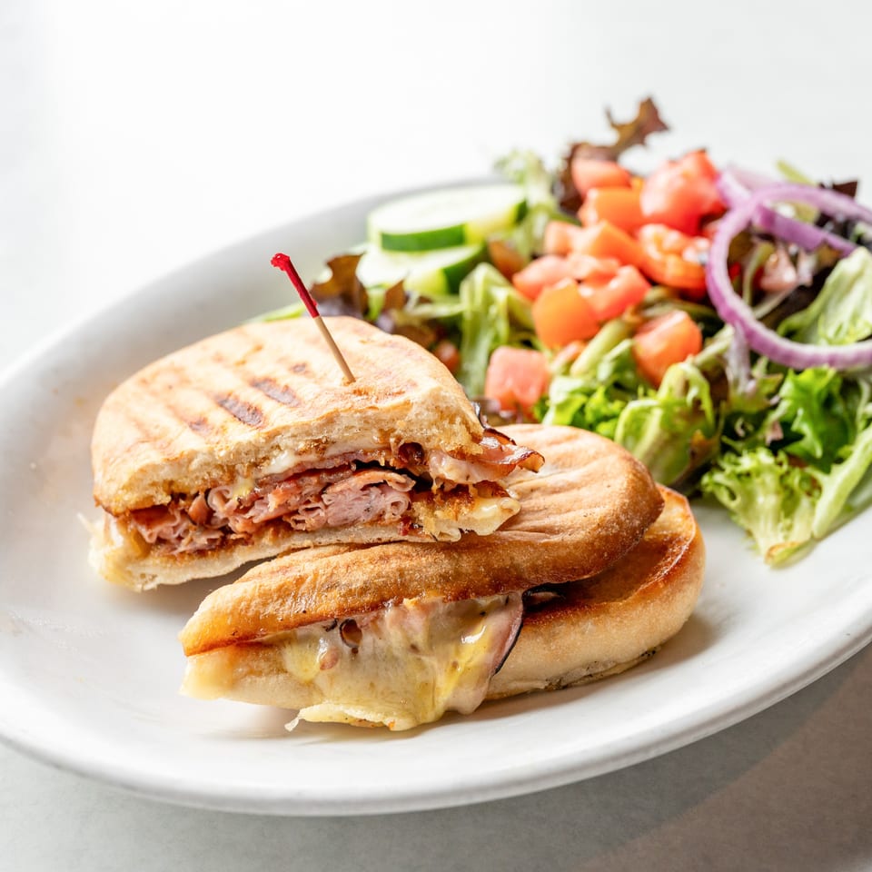 A grilled panini sandwich, cut in half, with melted cheese and meat, served with a side salad.