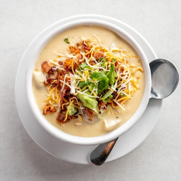 Creamy potato soup topped with shredded cheese, crispy bacon bits, and sliced green onions.