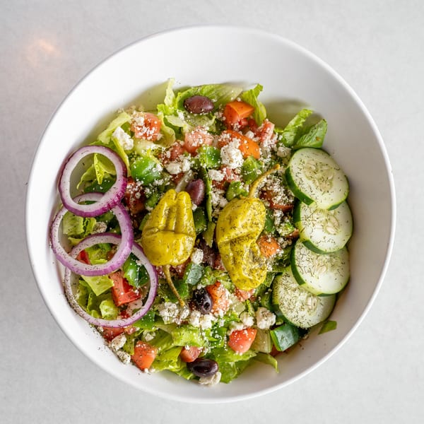 A vibrant Greek salad in a white bowl, featuring lettuce, tomatoes, cucumbers, red onions, feta, olives, and pepperoncini.