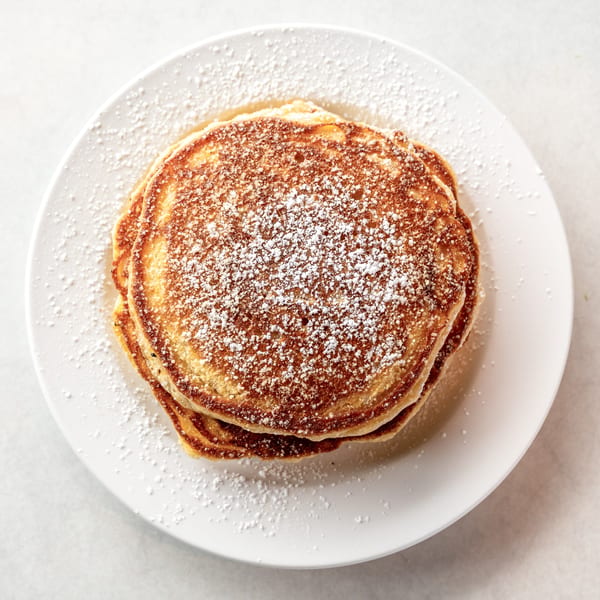 Stack of golden-brown pancakes dusted with powdered sugar on a white plate.
